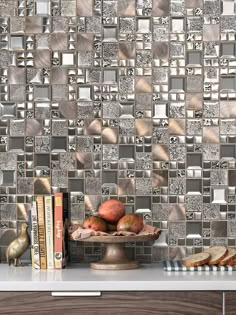 a table topped with books next to a wall covered in silver tiles and fruit on top of it