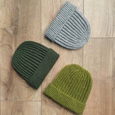 three knitted hats laying on the floor next to each other, one green and one grey