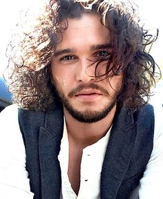 a man with long curly hair wearing a white shirt and black vest is looking at the camera