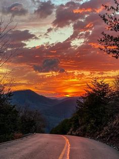 the sun is setting over mountains and trees on the side of the road in front of it