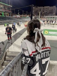 a woman standing on top of a metal railing next to an ice skating rink at night