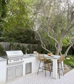 an outdoor kitchen with grill, table and chairs next to trees in the back yard