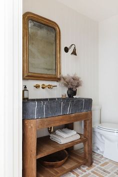 a white toilet sitting next to a wooden sink vanity in a bathroom under a mirror