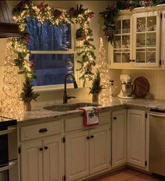 a kitchen decorated for christmas with lights and garland on the window sill over the sink