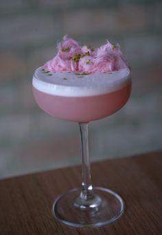 a pink cocktail in a wine glass with flowers on the rim and garnish