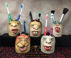 five ceramic faces with toothbrushes and makeup brushes in them, sitting on a table