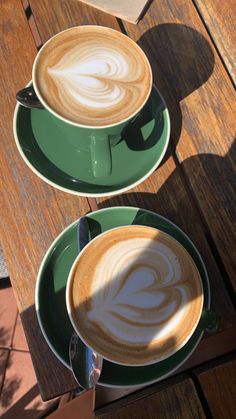 two cups of coffee sitting on top of green saucers with designs in the foam