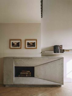 a fireplace with two framed pictures on the wall above it and some books in front of it