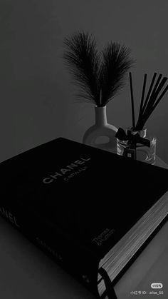 a black book sitting on top of a table next to a vase filled with reeds