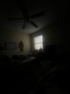 a dark room with a ceiling fan and window