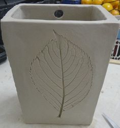 a planter with a leaf carved on the side sitting on top of a table