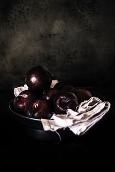 a metal bowl filled with plums on top of a black tablecloth covered surface