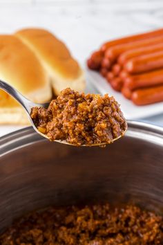 a spoon full of chili with hot dogs in the background