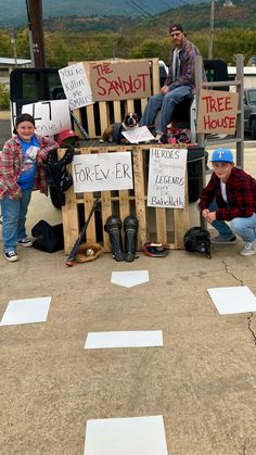 two boys and an adult sitting on top of a wooden crate with signs attached to it