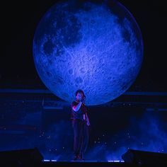 a man standing on top of a stage next to a giant moon