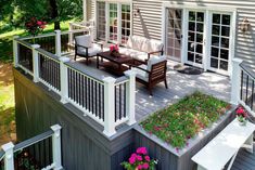 a deck with chairs, table and flowers in the planter boxes on it's side