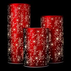 three red candles with white snowflakes and stars on them, sitting in front of a black background