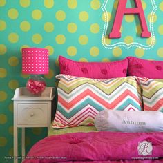 a bed with pink, green and yellow pillows on it in front of a polka dot wall