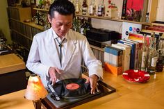 a man standing in front of a record player on top of a wooden table next to a lamp