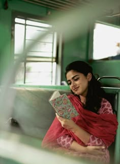 a woman sitting on a train holding a book in her hands and looking at the camera