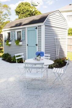 a white table and chairs sitting in front of a small shed with a blue door