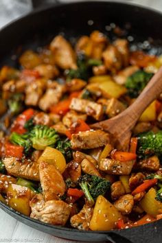 a skillet filled with chicken, broccoli and carrots next to a wooden spoon