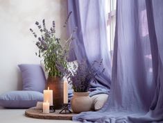 some candles are sitting on a table with lavenders in the background and blue drapes