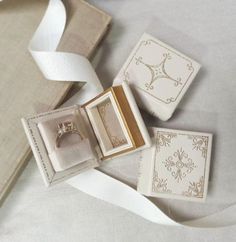 an open ring box sitting on top of a bed next to two boxes with wedding rings in them