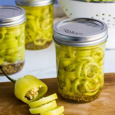 some pickles are sitting on a cutting board next to jars with food in them