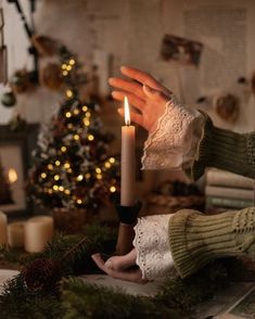 a person holding a lit candle in their hand next to a christmas tree and fireplace