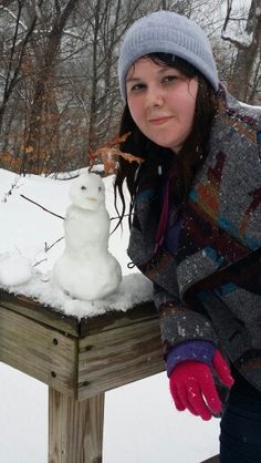 a woman standing next to a snowman on top of a wooden bench