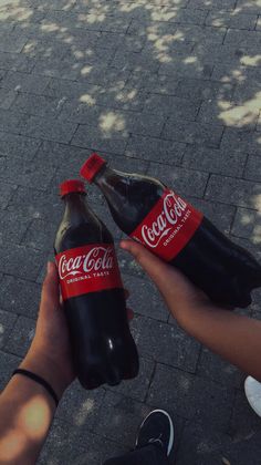 two bottles of coca - cola sitting on the ground next to someone's feet