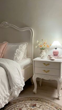 a white bed sitting next to a nightstand with flowers on it and a pink lamp