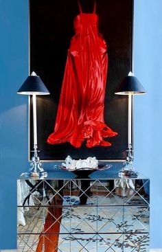 the reflection of a woman's red dress in a mirrored cabinet with two lamps