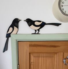 two black and white birds on top of a door with a clock in the background