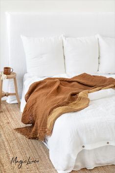 a bed with white linens and brown blankets on it, in a bedroom setting