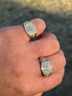 a man's hand holding two rings with diamonds on them and the middle one in yellow gold