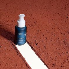 a bottle of lotion sitting on top of a red dirt field next to a white line