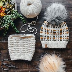 three knitted hats and two crochet hooks on a wooden surface