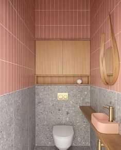 a bathroom with pink and grey tiles on the walls, wood cabinet above the toilet