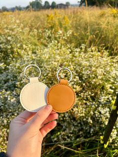 a hand holding two leather key fobs in front of some wildflowers