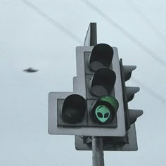 a traffic light with an alien sticker on it's face and two birds flying in the background