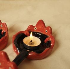 two red ceramic objects with a lit candle in the shape of cats sitting on top of each other