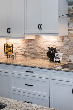 a black cat sitting on top of a kitchen counter next to a white cupboards