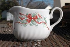 a white pitcher with red bows painted on it's side sitting on a table