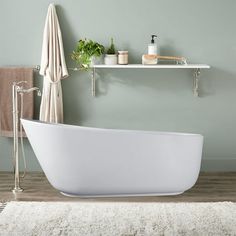 a white bathtub sitting on top of a wooden floor next to a shelf filled with plants