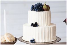 a three tiered white cake with blueberries and figurines on the top