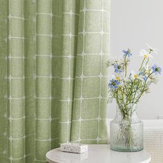 a vase with flowers on a table next to a curtain