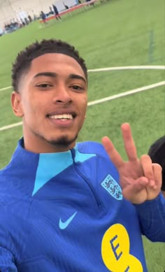 a young man making the peace sign with his hand on a soccer field in front of him