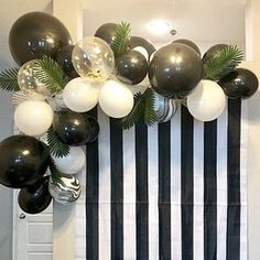 black and white balloons are hanging on the wall in front of a striped backdrop with palm leaves